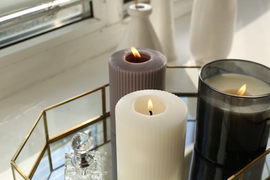 Different burning candles, perfume and vases on window sill