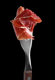 Tasty prosciutto on fork against black background