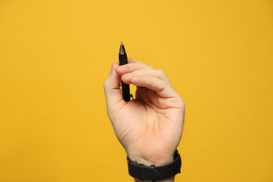 Photo of Left-handed man holding pen on yellow background, closeup