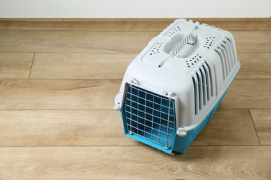 Photo of Light blue pet carrier on floor indoors. Space for text