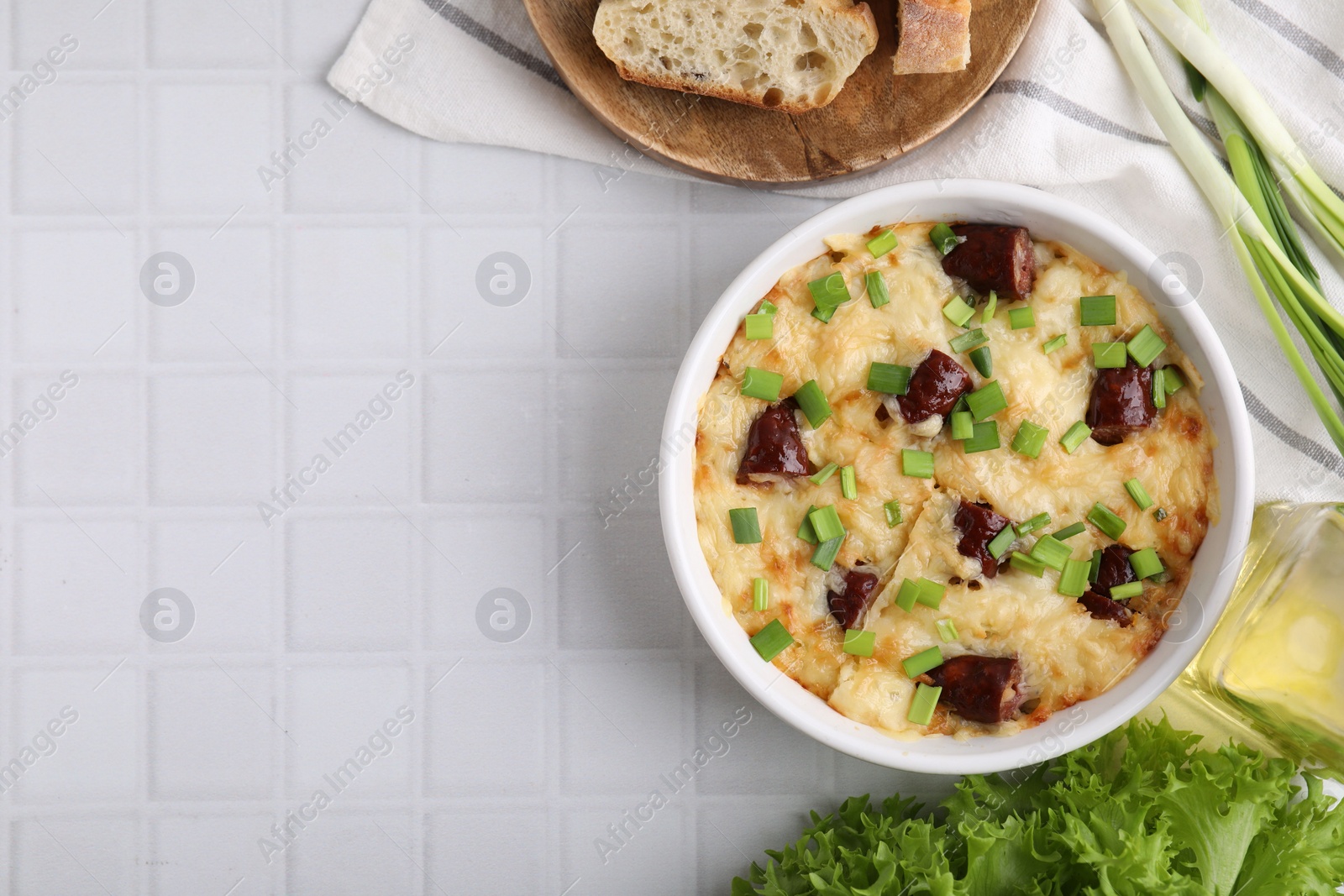 Photo of Tasty sausage casserole in baking dish served on white tiled table, flat lay. Space for text