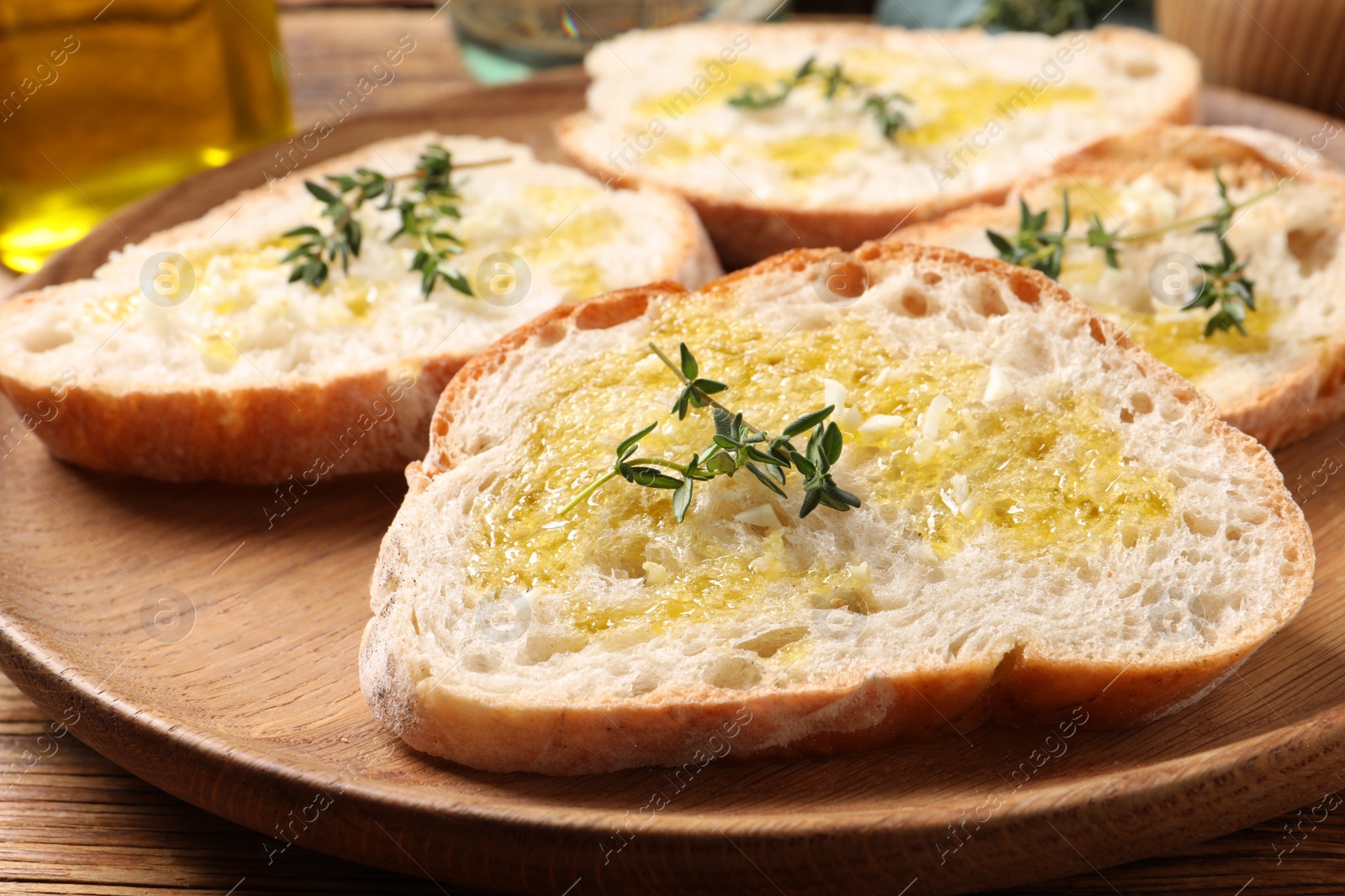 Photo of Tasty bruschettas with oil and thyme on wooden plate, closeup