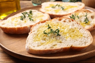 Photo of Tasty bruschettas with oil and thyme on wooden plate, closeup