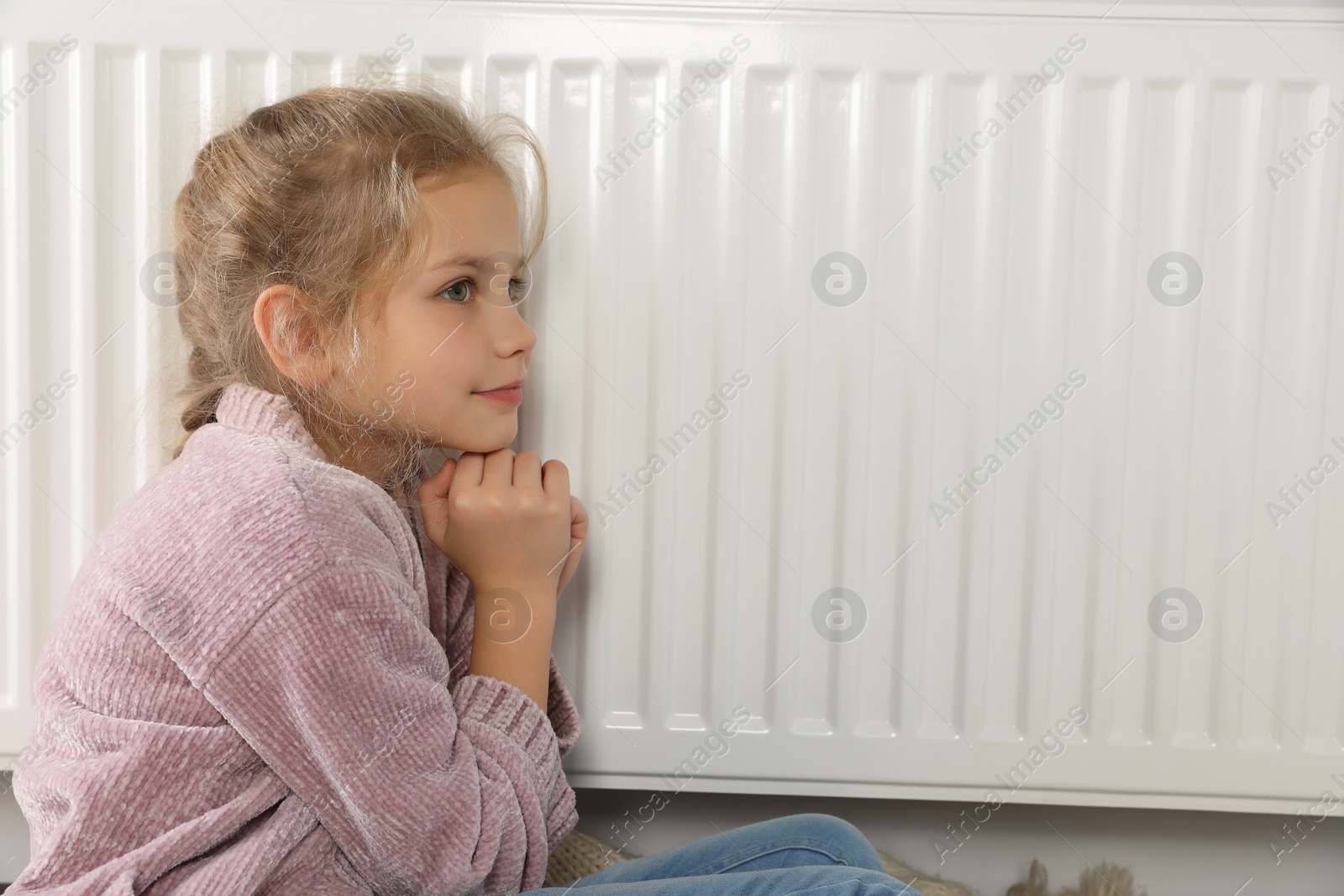 Photo of Little girl near heating radiator at home, space for text