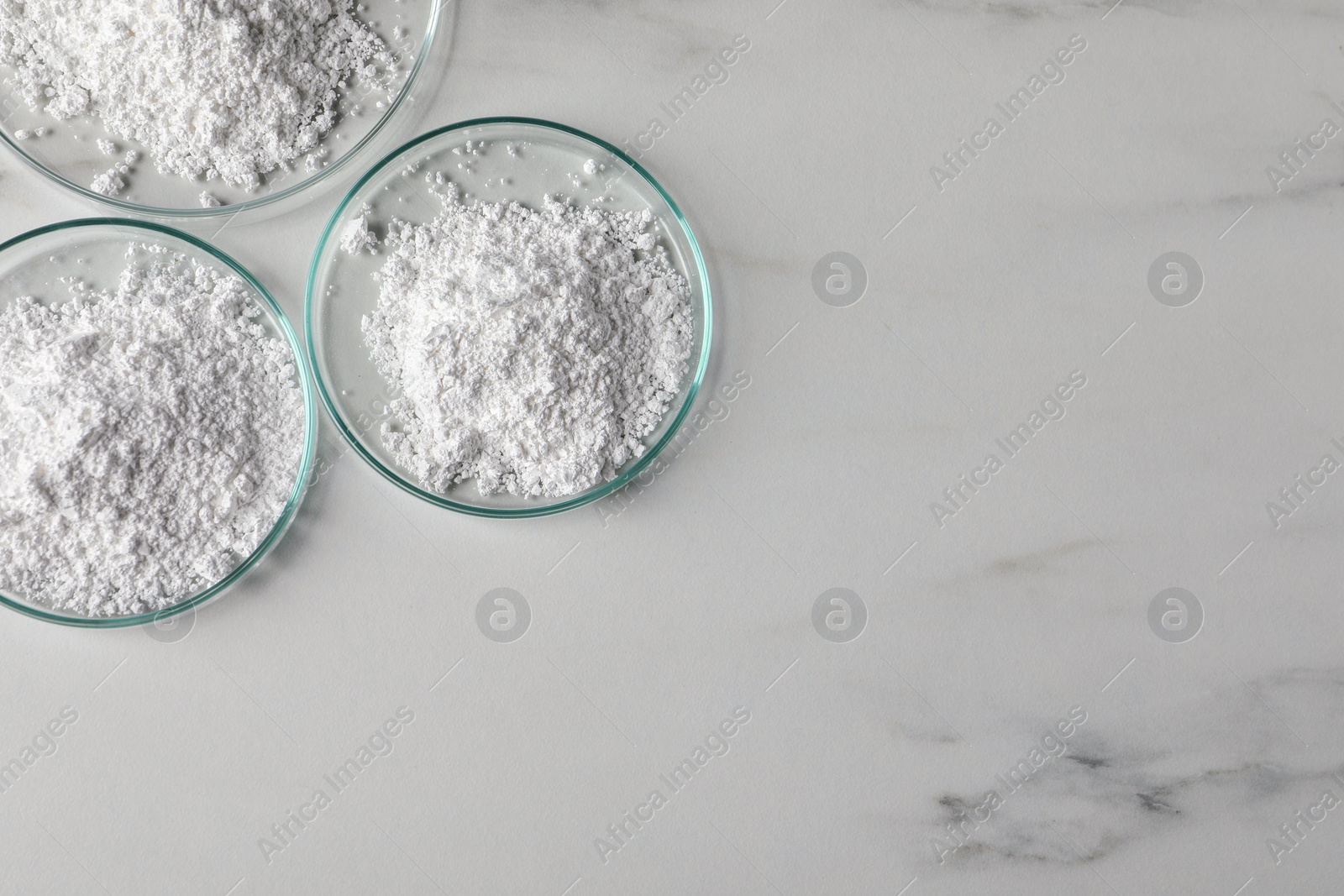 Photo of Petri dishes with calcium carbonate powder on white marble table, flat lay. Space for text
