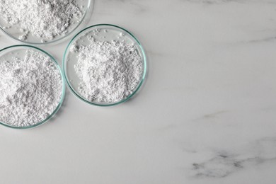 Photo of Petri dishes with calcium carbonate powder on white marble table, flat lay. Space for text