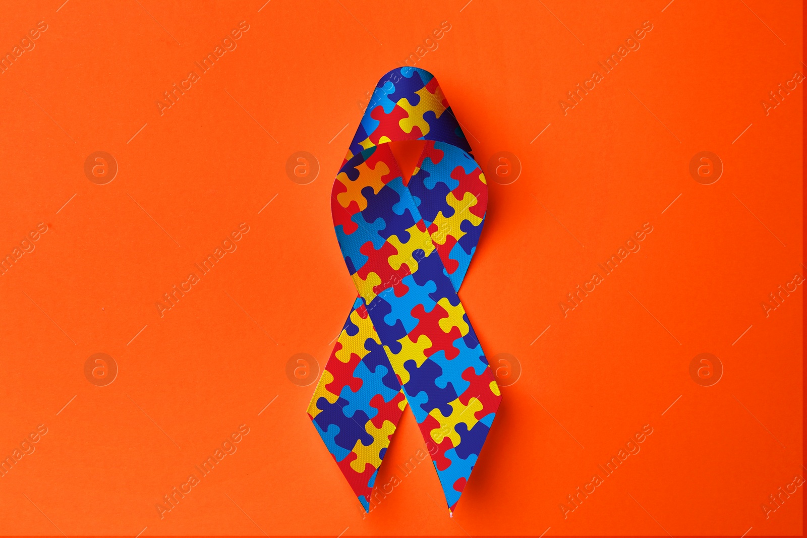 Image of World Autism Awareness Day. Colorful puzzle ribbon on orange background, top view