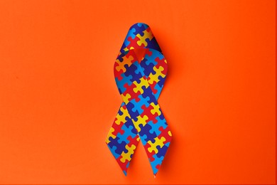 Image of World Autism Awareness Day. Colorful puzzle ribbon on orange background, top view