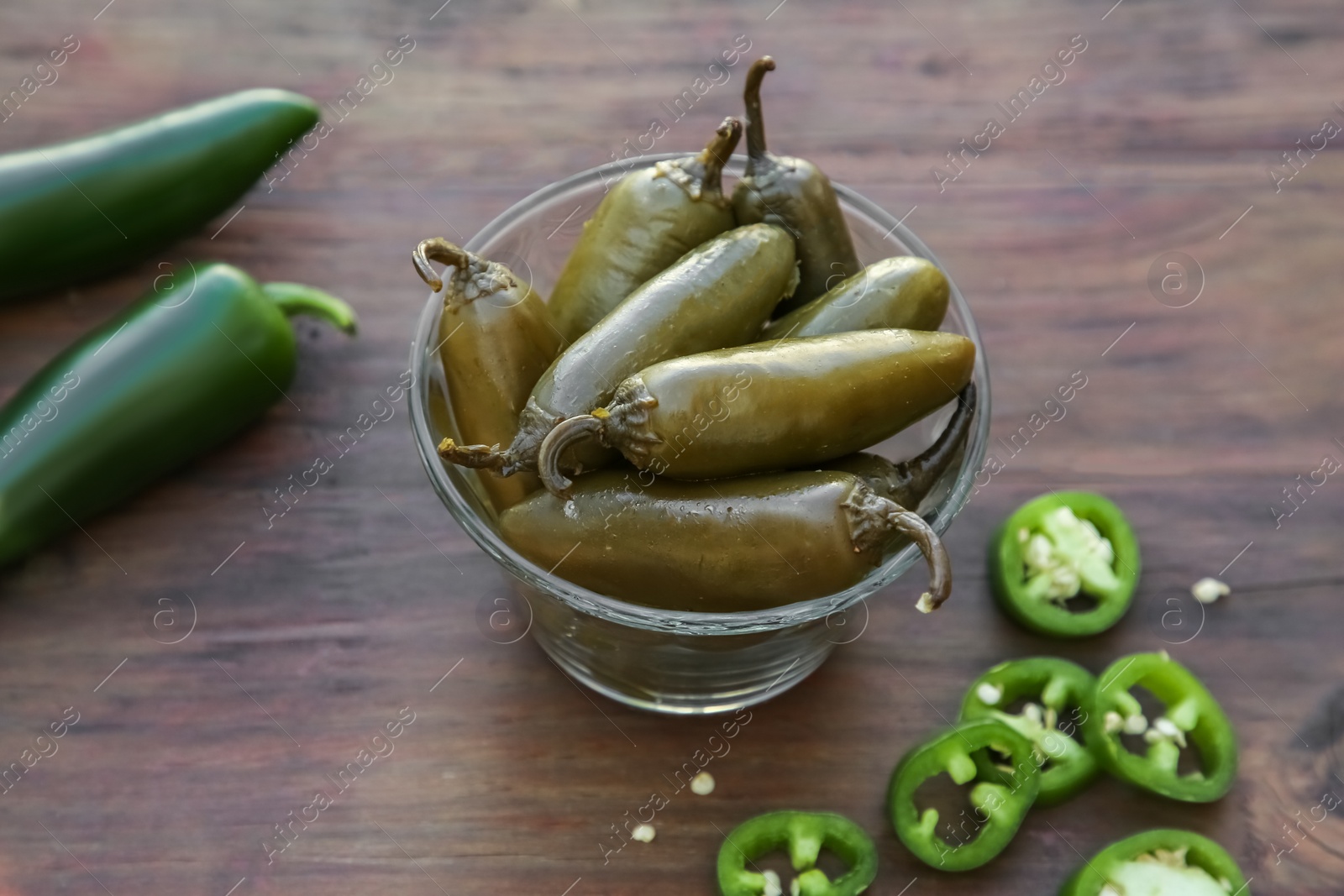 Photo of Fresh and pickled green jalapeno peppers on wooden table