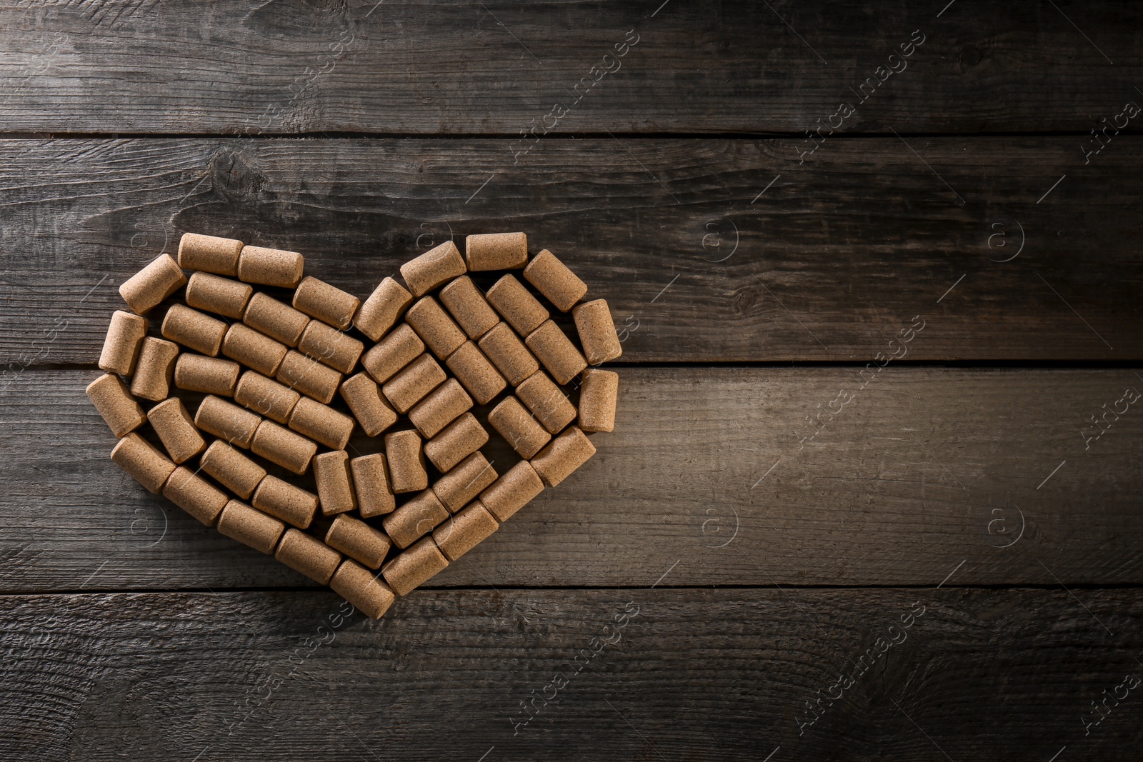 Photo of Heart made of wine bottle corks on wooden table, top view. Space for text