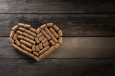 Photo of Heart made of wine bottle corks on wooden table, top view. Space for text