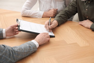 Photo of Notary showing senior couple where to sign Last Will and Testament at wooden table indoors, closeup