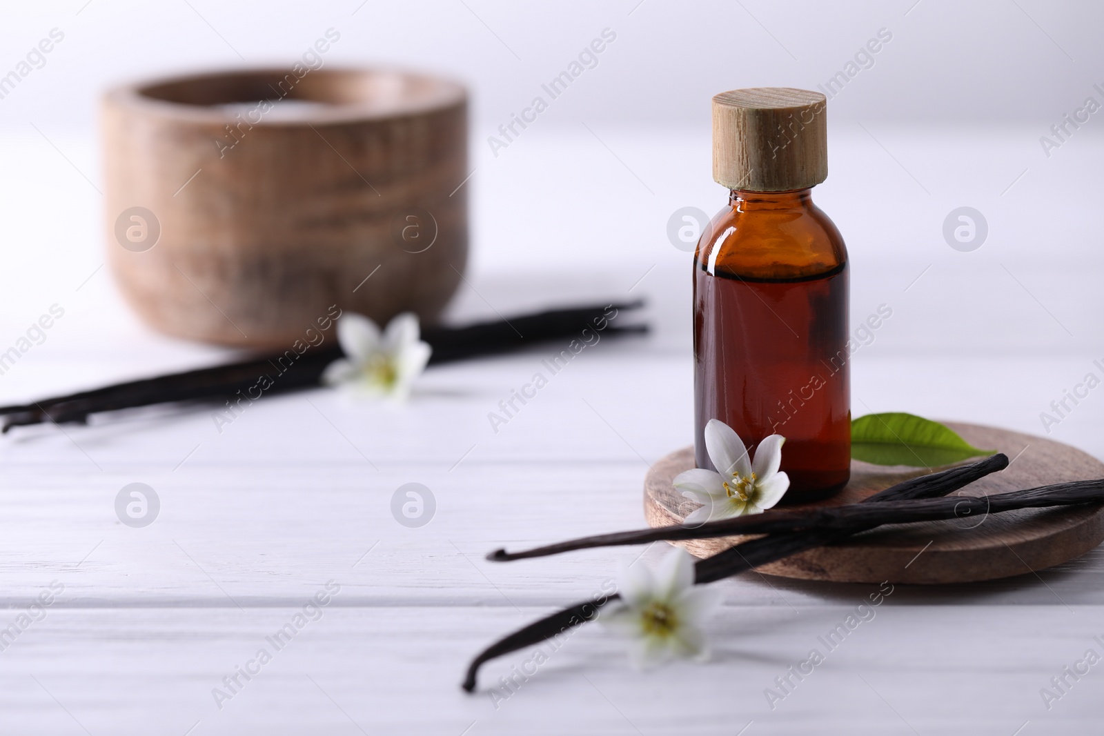 Photo of Vanilla pods, flowers, leaf and bottle with essential oil on white wooden table, closeup