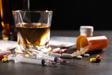 Photo of Alcohol and drug addiction. Syringes, whiskey in glass and pills on grey table, closeup