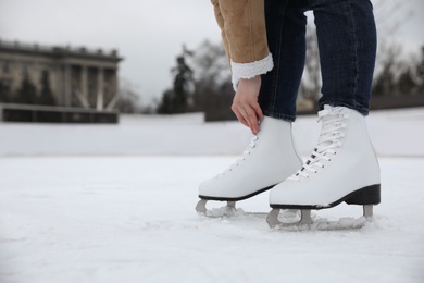 Woman lacing figure skate on ice rink, closeup. Space for text