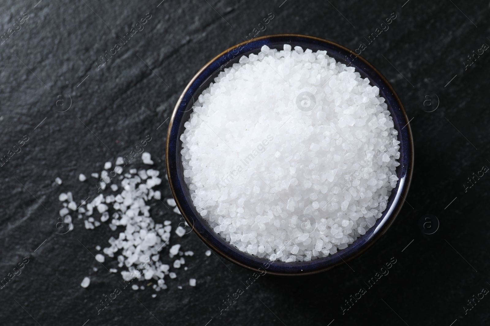 Photo of Organic white salt in bowl on black table, top view