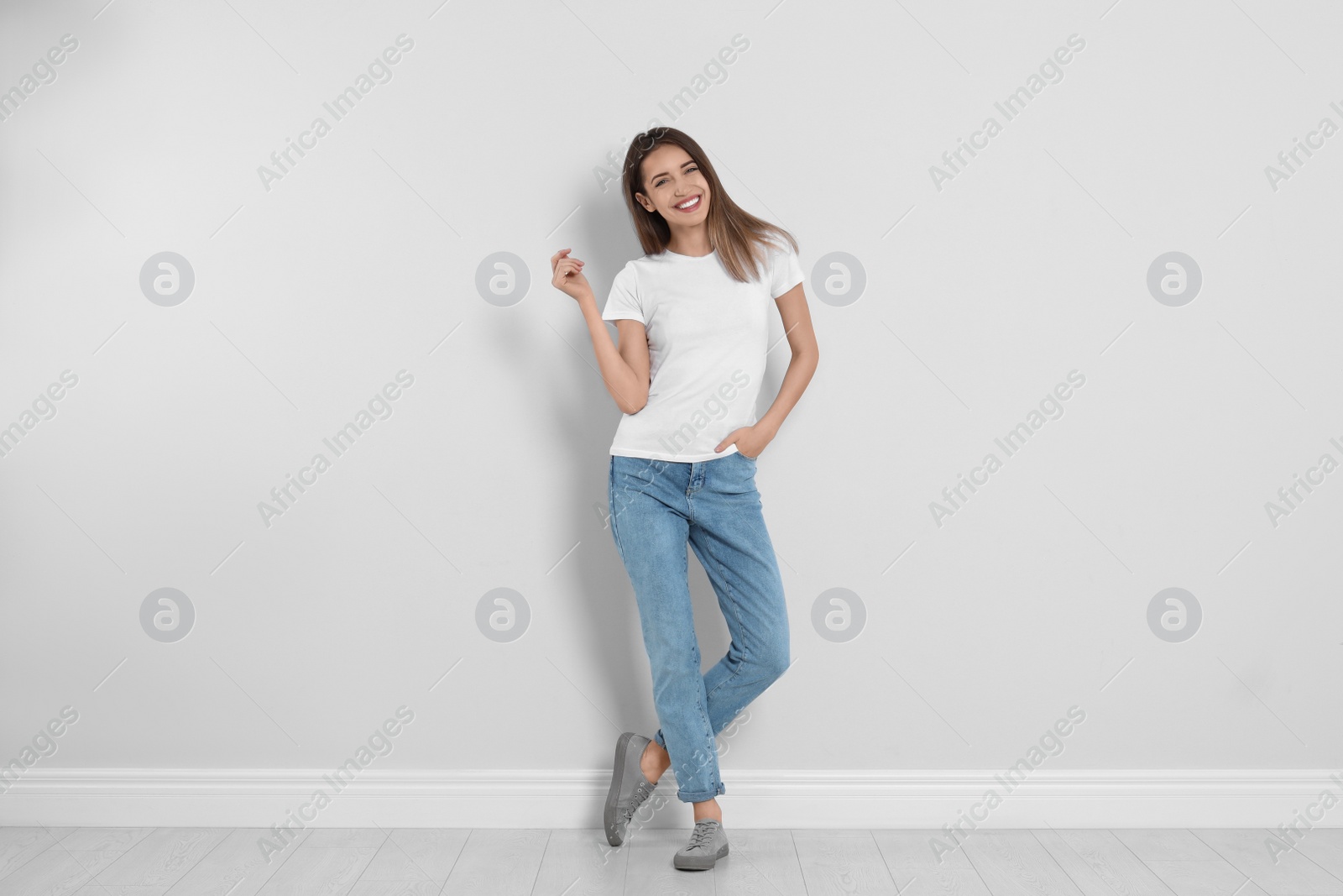 Photo of Young woman in stylish jeans near light wall