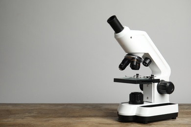 Modern microscope on wooden table against grey background, space for text. Medical equipment