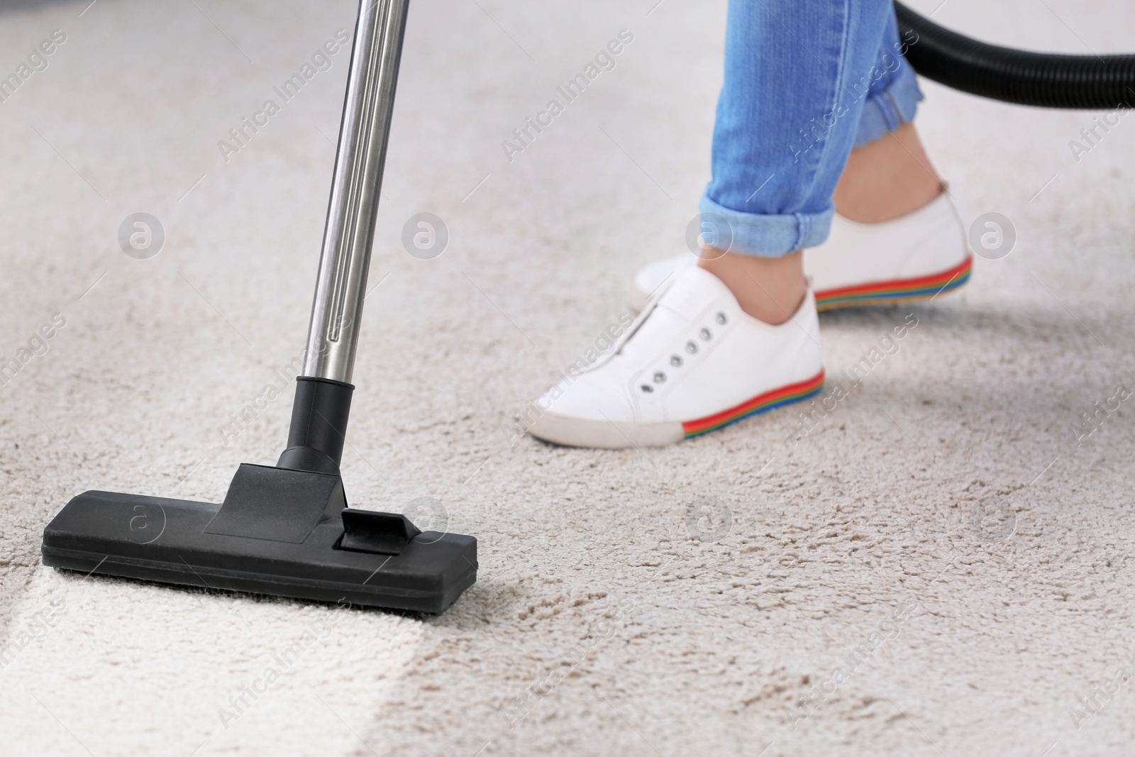 Photo of Woman removing dirt from carpet with vacuum cleaner indoors, closeup