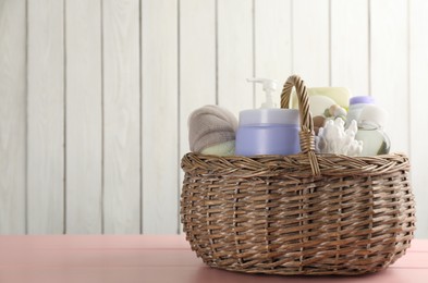 Photo of Wicker basket full of different baby cosmetic products and bathing accessories on pink wooden table. Space for text