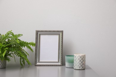 Empty photo frame, candles and green plant on grey table