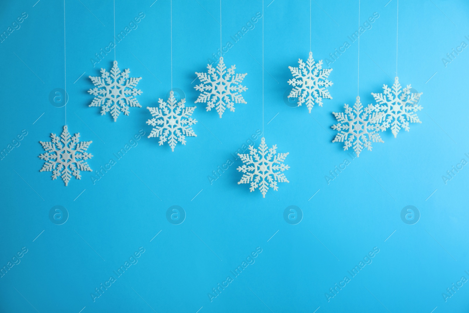 Photo of Beautiful decorative snowflakes hanging on light blue background