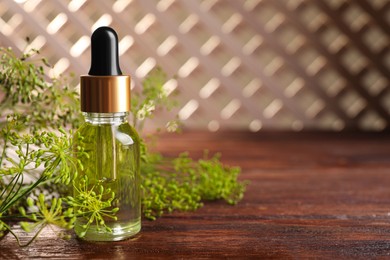 Photo of Bottle of essential oil and fresh dill on wooden table, closeup. Space for text