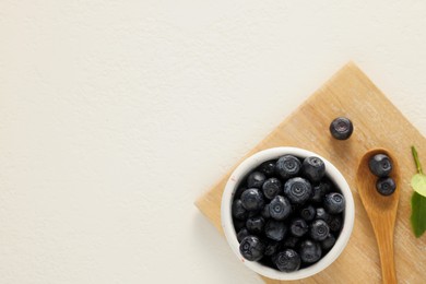 Photo of Ripe bilberries and leaves on white table, top view. Space for text