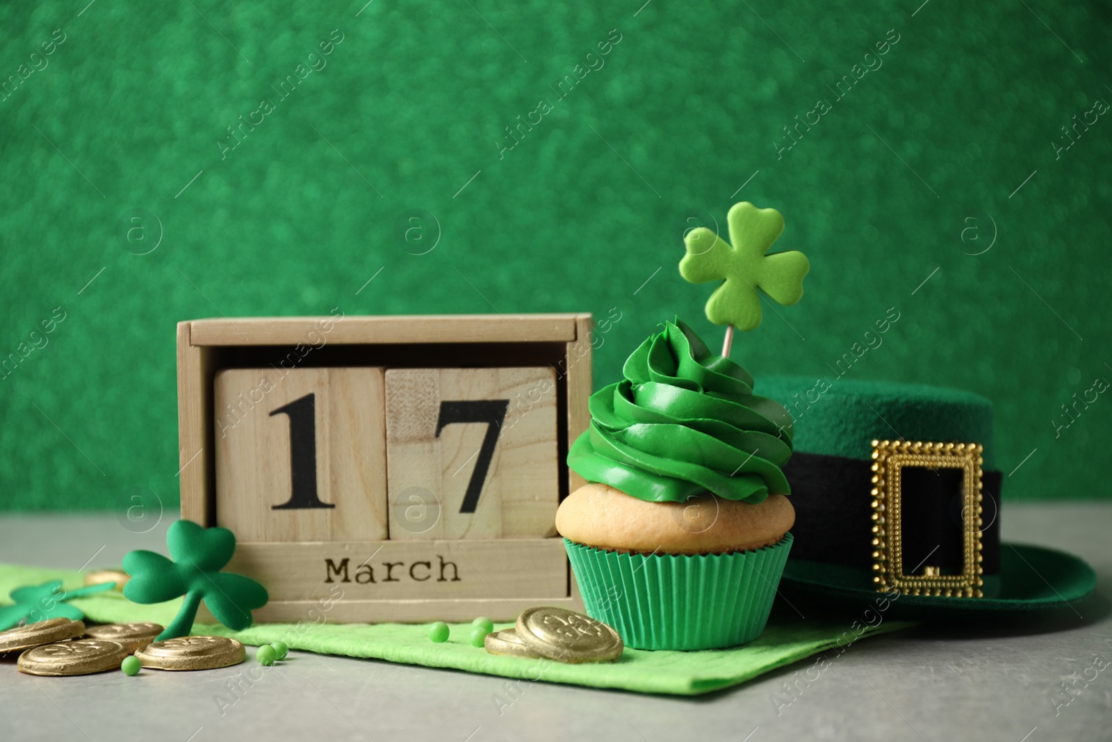 Photo of Decorated cupcake, wooden block calendar, hat and coins on grey table. St. Patrick's Day celebration
