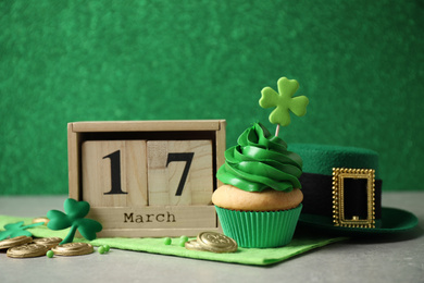 Decorated cupcake, wooden block calendar, hat and coins on grey table. St. Patrick's Day celebration