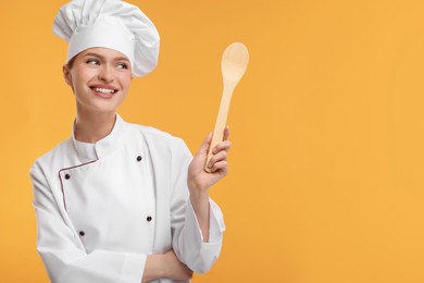 Photo of Happy woman chef in uniform holding wooden spoon on orange background, space for text