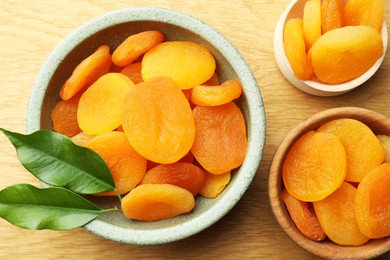 Photo of Tasty apricots with green leaves on wooden table, flat lay. Dried fruits