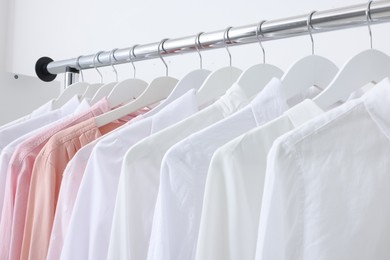 Rack with different stylish shirts near white wall, closeup. Organizing clothes