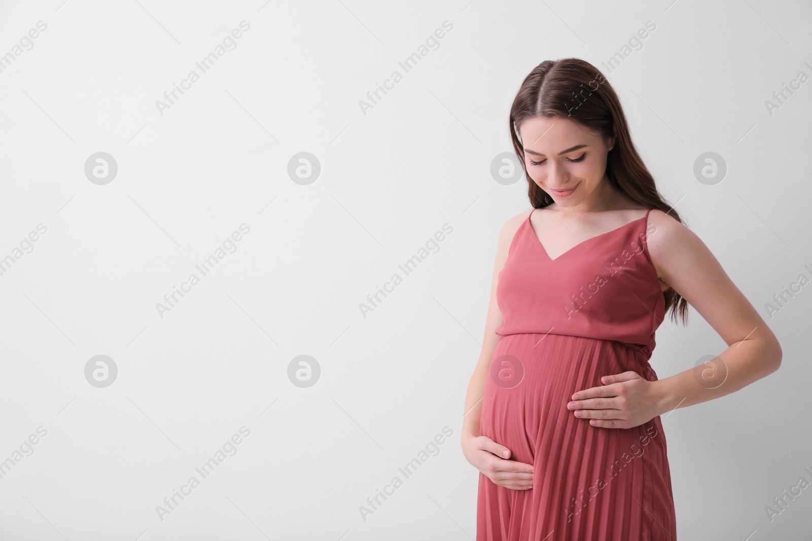 Photo of Beautiful young pregnant woman on light background. Space for text