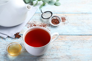 Photo of Freshly brewed rooibos tea and honey on light wooden table. Space for text