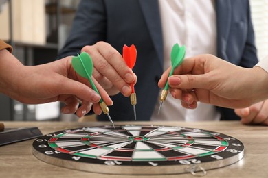 Photo of Business targeting concept. People with darts aiming at dartboard at table indoors, closeup