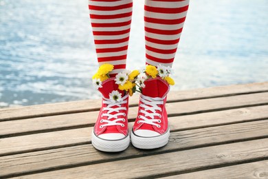 Photo of Woman with beautiful tender flowers in socks on wooden pier, closeup