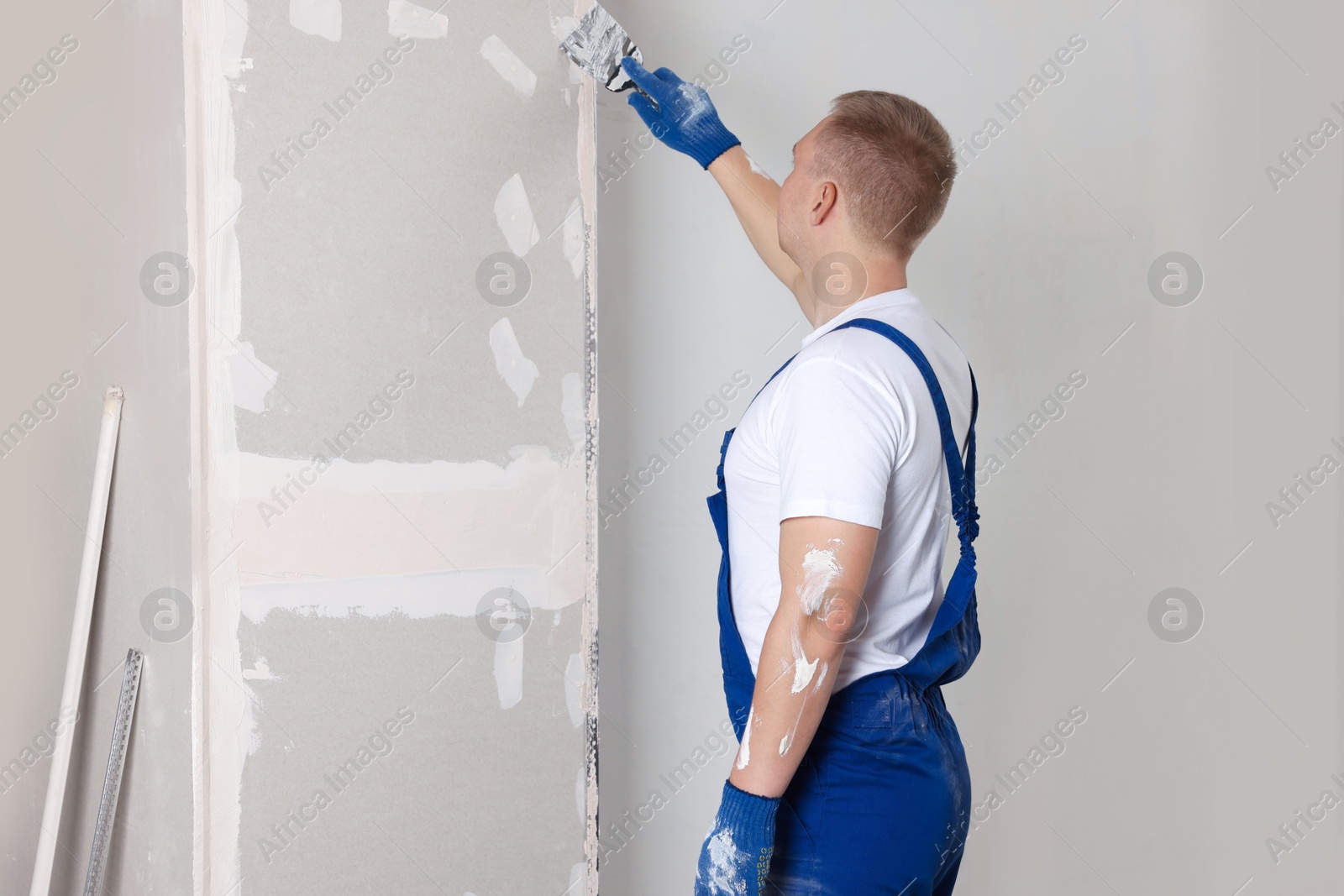 Photo of Man plastering wall with putty knife indoors. Home renovation