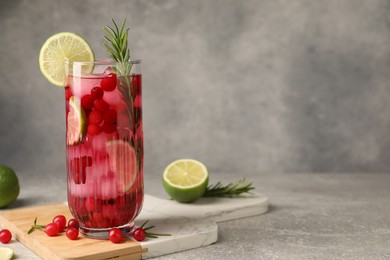 Photo of Tasty cranberry cocktail with rosemary and lime in glass on gray textured table, space for text