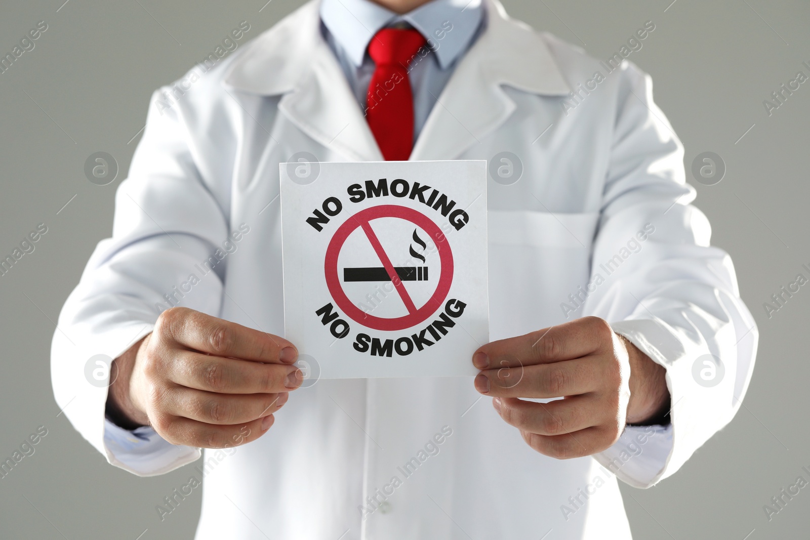 Photo of Doctor holding card with no smoking sign on gray background, closeup