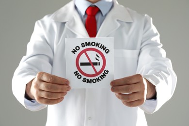 Photo of Doctor holding card with no smoking sign on gray background, closeup