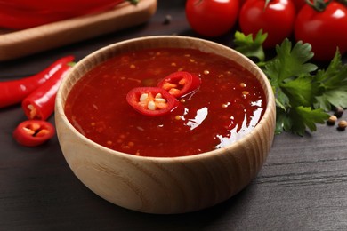 Photo of Spicy chili sauce in bowl on wooden table, closeup