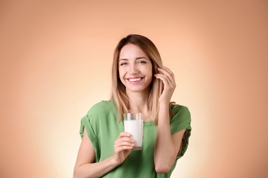 Beautiful young woman drinking milk on color background