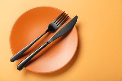 Photo of Ceramic plate with cutlery on pale orange background, top view. Space for text