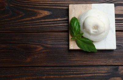 Photo of Delicious burrata cheese with basil on wooden table, top view. Space for text