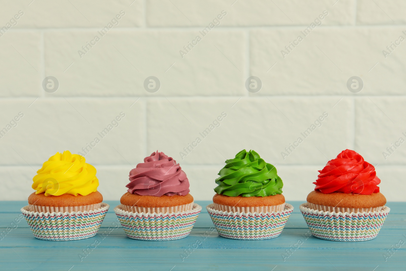 Photo of Delicious cupcakes with colorful cream on light blue wooden table
