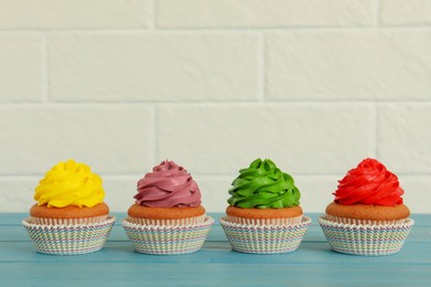 Delicious cupcakes with colorful cream on light blue wooden table
