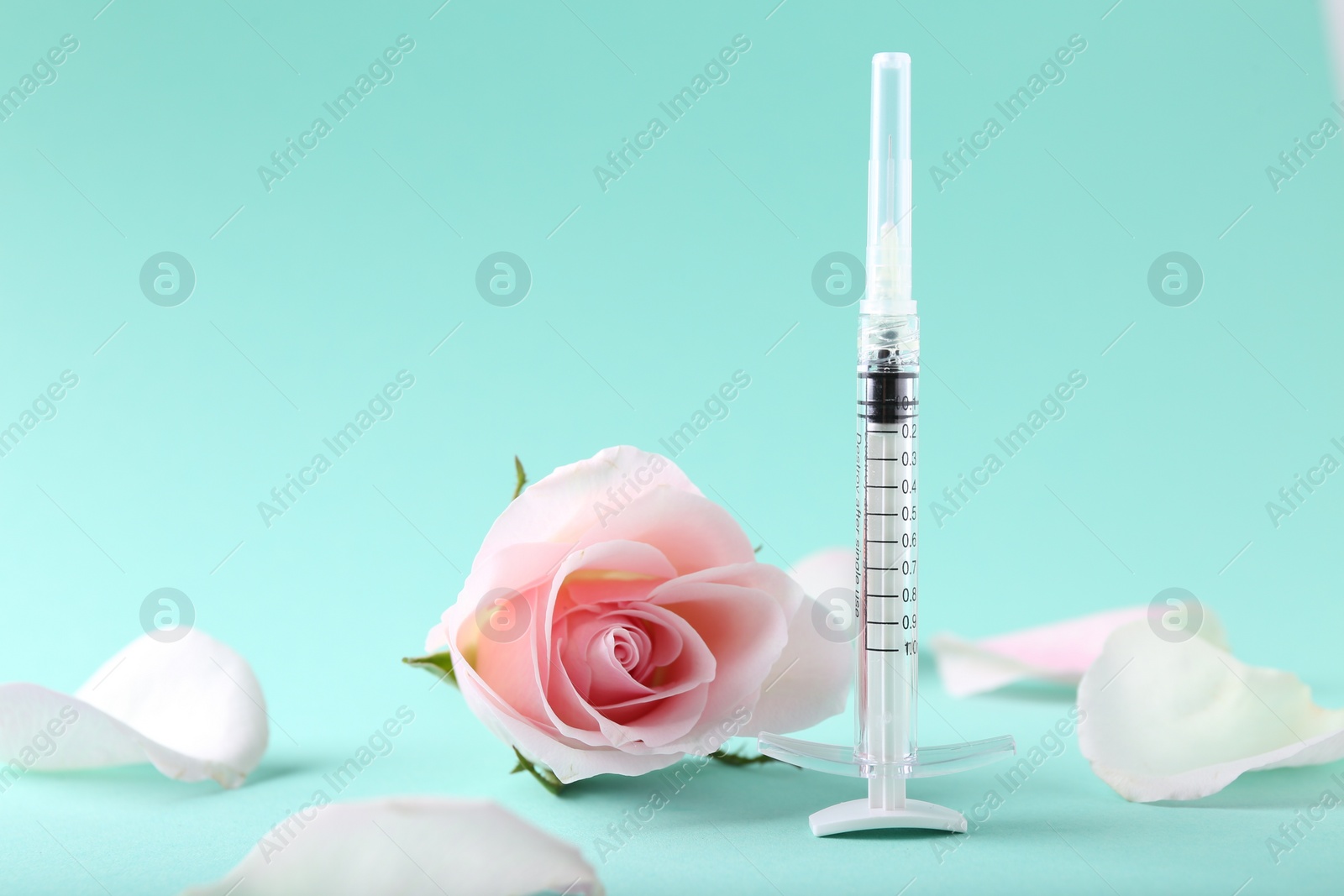 Photo of Cosmetology. Medical syringe, rose flower and petals on turquoise background, space for text