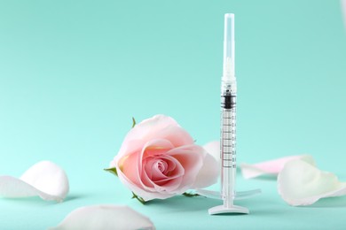 Cosmetology. Medical syringe, rose flower and petals on turquoise background, space for text