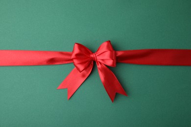 Photo of Red satin ribbon with bow on green background, top view